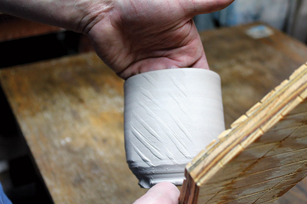 3 Place one hand on the inside of a leather-hard pot for support, then paddle the exterior of the pot to alter its surface.