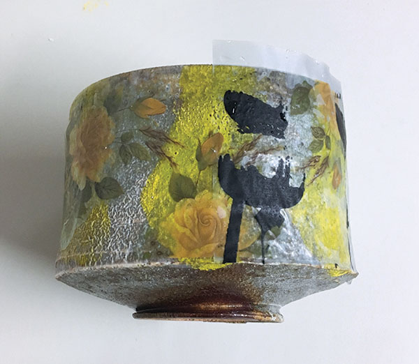 Various decals applied in a layered fashion with yellow roses first, then black decals applied on top. Ready to be refired again to cone 010.
